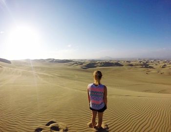 Rear view of woman standing on sand dunes against sky at sahara desert