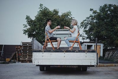 People having coffee while sitting on chair in land vehicle against trees