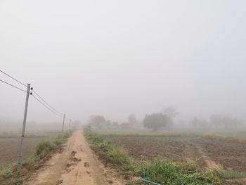 Dirt road amidst field against sky during foggy weather