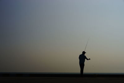 Silhouette man fishing against sky during sunset
