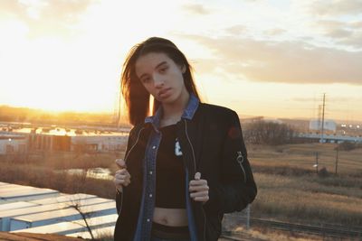 Young woman using smart phone against sky during sunset