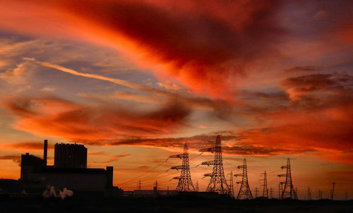 Low angle view of silhouette factory against dramatic sky