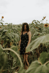 Young woman standing amidst sunflowers on field against sky