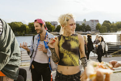 Smiling non-binary person with gay friend on promenade in city