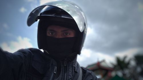 Close-up portrait of man wearing helmet against sky