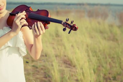 Midsection of woman playing violin on field