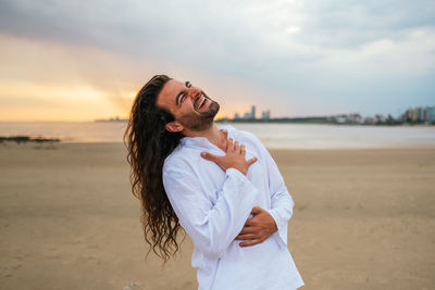 Young woman standing on beach against sky during sunset