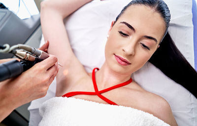 From above beautician removing hair from armpit of female customer during laser epilation procedure in aesthetic clinic