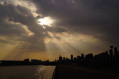 Silhouette of city against cloudy sky during sunset