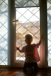 Rear view of girl looking through window at home