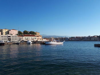 Sailboats in sea by buildings against clear blue sky