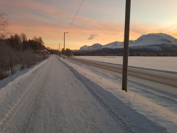 Road by snowcapped mountains against sky during sunset