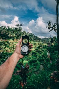 Cropped hand of man holding navigational compass against trees