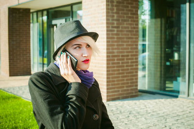 Young woman talking on mobile phone by built structure