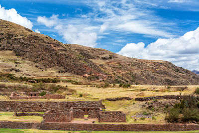 Incan ruins of tipon by mountains against cloudy sky