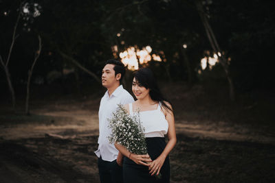 Smiling young woman with white flowers standing by man