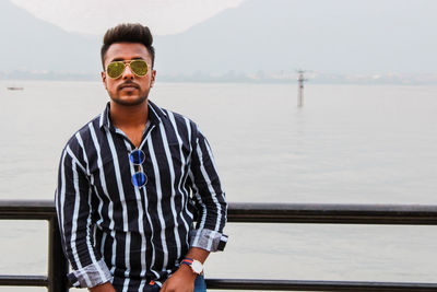 Portrait of young man standing against railing