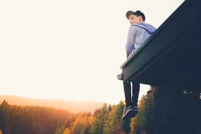 Low angle view of young man sitting on rooftop