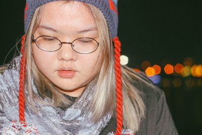 Close-up of young woman in warm clothing looking down while sitting against sky at night