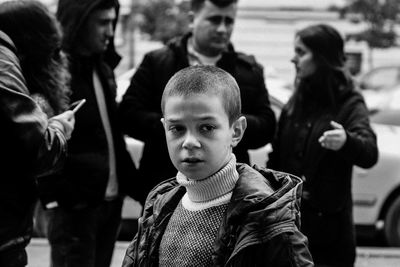 Boy looking away while standing with people in city