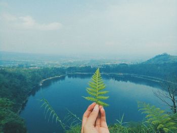 Hand by lake against sky