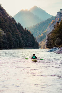 People in boat on river against mountains