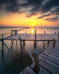 Wooden posts in sea against sky during sunset