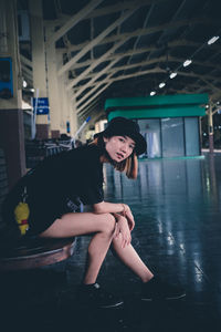 Full length of young woman sitting at railroad station platform