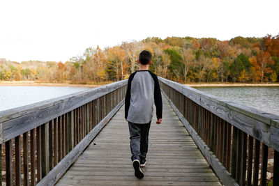 Rear view of man on footbridge over lake
