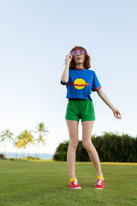Portrait of smiling woman standing on grass against clear sky