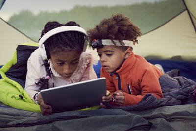 Brother and sister lying in tent while using digital tablet