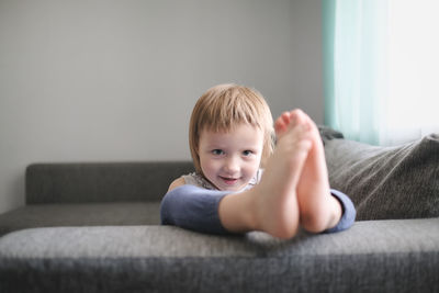 Child jumps and plays on sofa in minimalist living room, gray sofa.