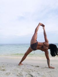 Rear view of woman in bikini stretching at beach