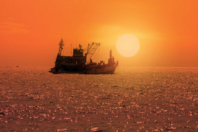 Silhouette of fishing boat in the sea with colorful sunset background.