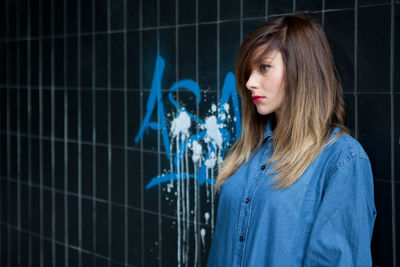 Young woman wearing blue shirt while looking away against wall