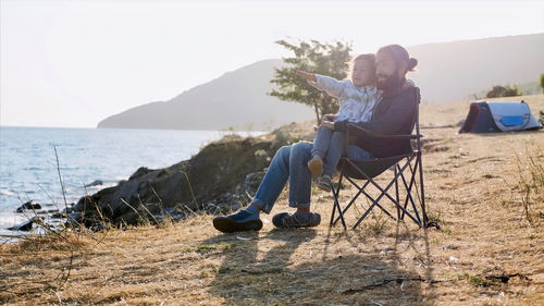 Men sitting on shore at beach against sky