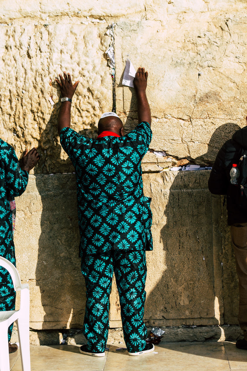 REAR VIEW OF MAN STANDING AGAINST WALL