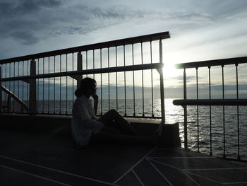 Side view of woman sitting on railing against sea