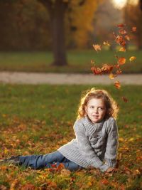 Smiling girl sitting in park during autumn