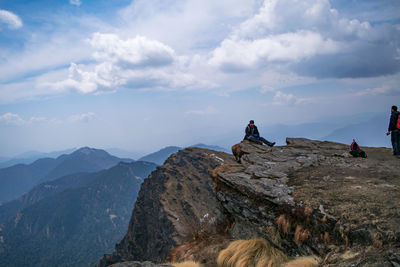People sitting on rock by mountains against sky