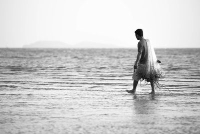 Side view of fisherman carrying fishing net and walking on wet beach