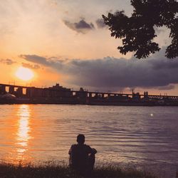 Rear view of man looking at sunset over river