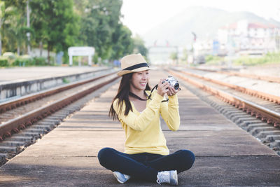 Woman photographing while sitting on railroad track