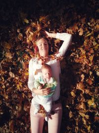 High angle view of baby boy lying on mother against autumn leaves