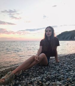 Young woman sitting on rock at beach against sky