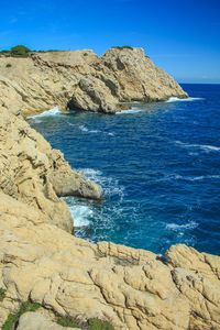 Scenic view of rocks by sea against blue sky