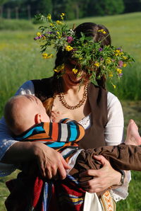 Beautiful woman wearing flowers carrying baby boy on sunny day