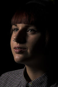 Close-up of thoughtful young woman with braces against black background
