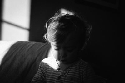 Cute baby girl looking down while sitting on sofa in darkroom