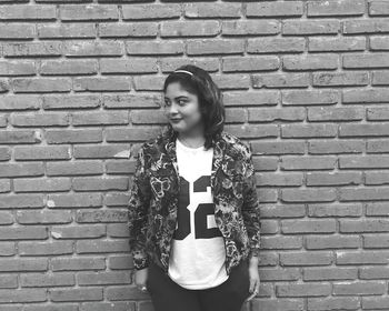 Portrait of young woman standing on brick wall